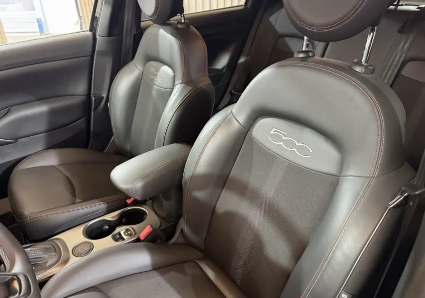 Gros plan sur les sièges avant noirs en cuir et tissu de la Fiat 500X 2021 avec logo 500 brodé et surpiqûres rouges.