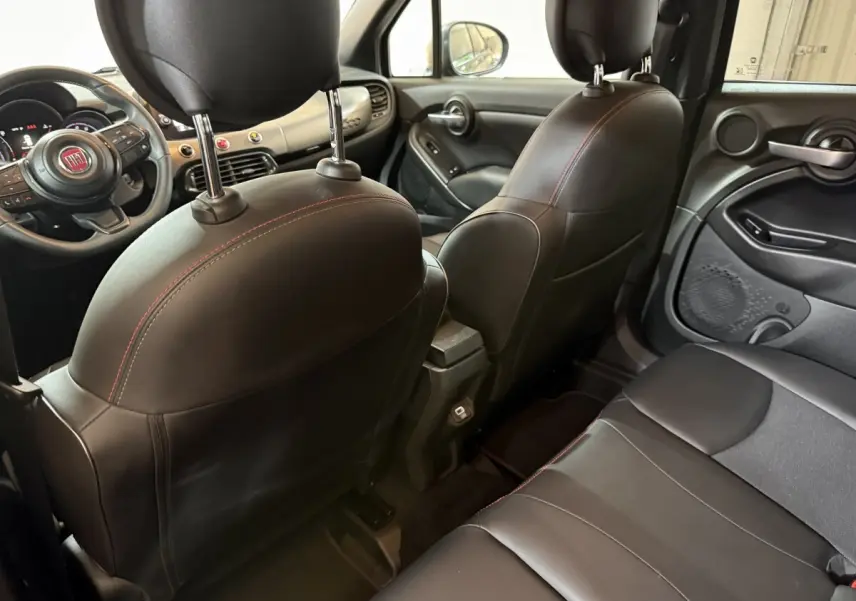 Intérieur arrière noir de la Fiat 500X 2021, vue depuis la banquette arrière vers les sièges avant en cuir avec surpiqûres rouges.