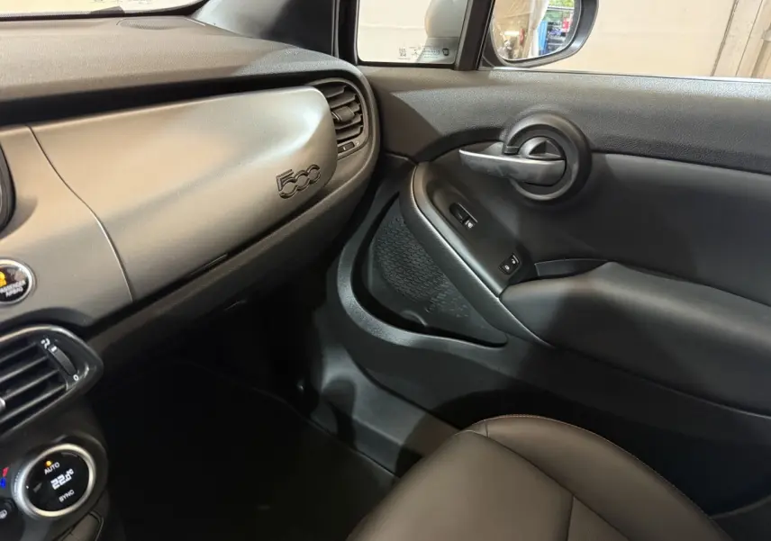 Vue intérieure côté passager du tableau de bord noir mat et de la portière avec logo 500 visible sur une FIAT 500X 2021.