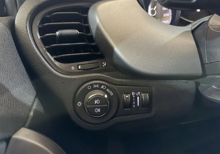 Gros plan sur la commande des phares et la sortie d’air à gauche du tableau de bord noir du Fiat 500X 2021.