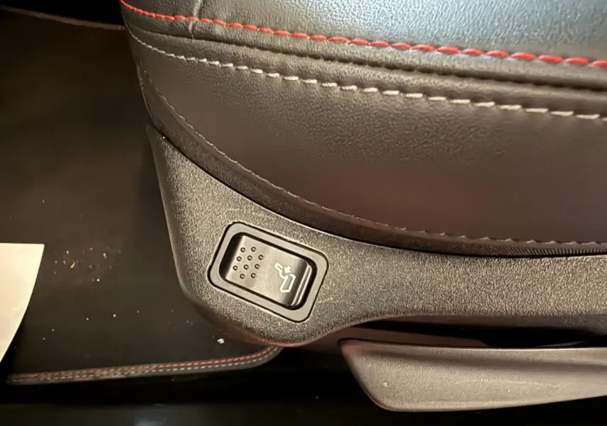 Gros plan sur le bouton de réglage de siège avec surpiqûres rouges sur cuir noir dans une Fiat 500X 2021 Sport.