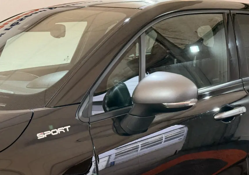 Vue rapprochée du côté gauche d'une FIAT 500X noire avec logo Sport et rétroviseur argenté mat.