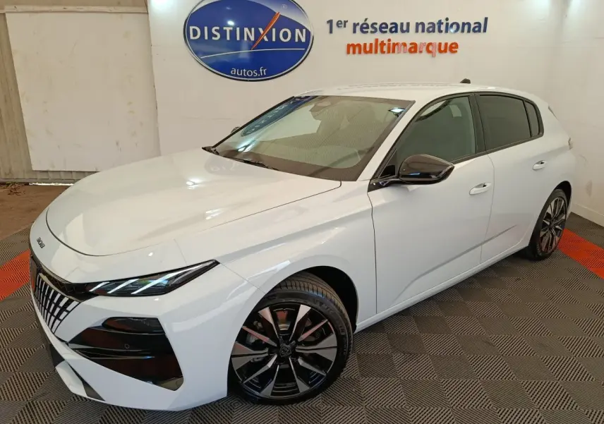 Peugeot 308 blanc vue 3/4 avant droit, avec jantes alliage noires et calandre distinctive en showroom.