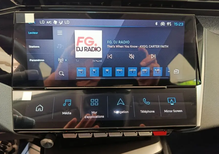 Écran tactile central de la Peugeot 308 blanc, affichant la radio FG DJ Radio avec commandes multimédia.