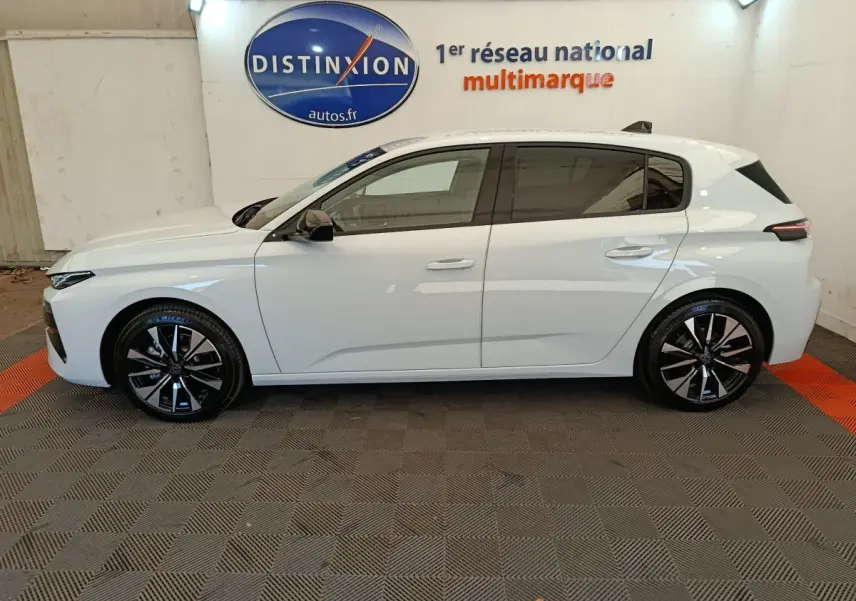 Vue de profil côté gauche d'une Peugeot 308 blanche 2026 dans un showroom avec jantes noires et logo Distinxion en arrière-plan.