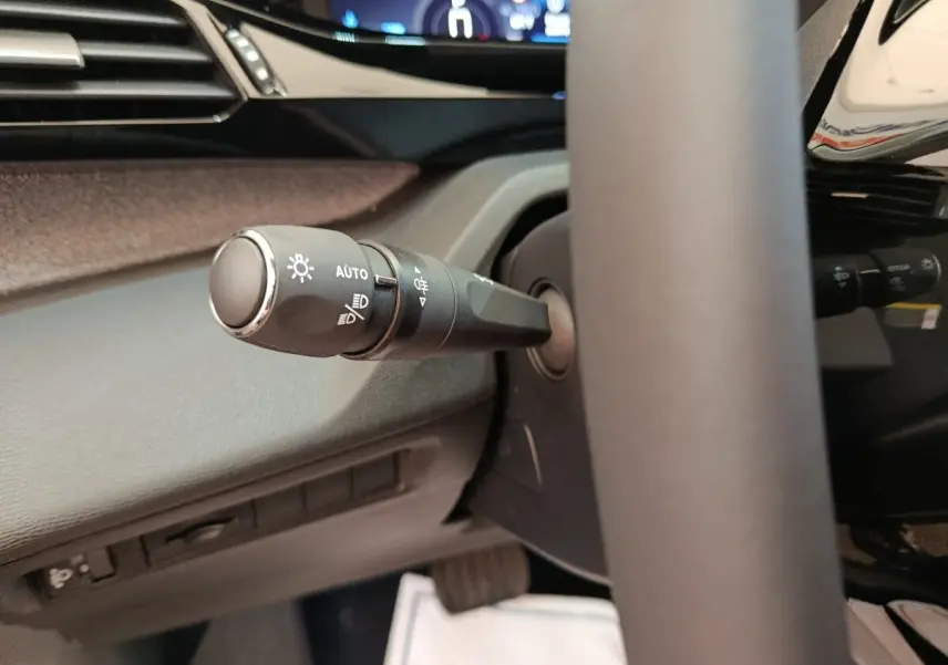 Gros plan sur la commande des feux à gauche du volant cuir dans l’habitacle sombre de la Peugeot 308 blanche 2026.