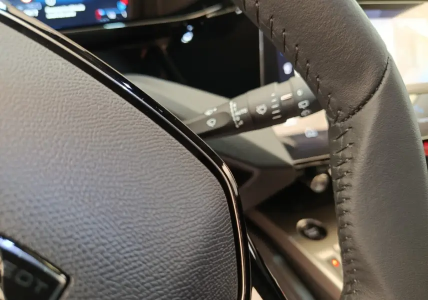 Gros plan sur le volant cuir gris de la Peugeot 308 2026, avec tableau de bord numérique en arrière-plan.
