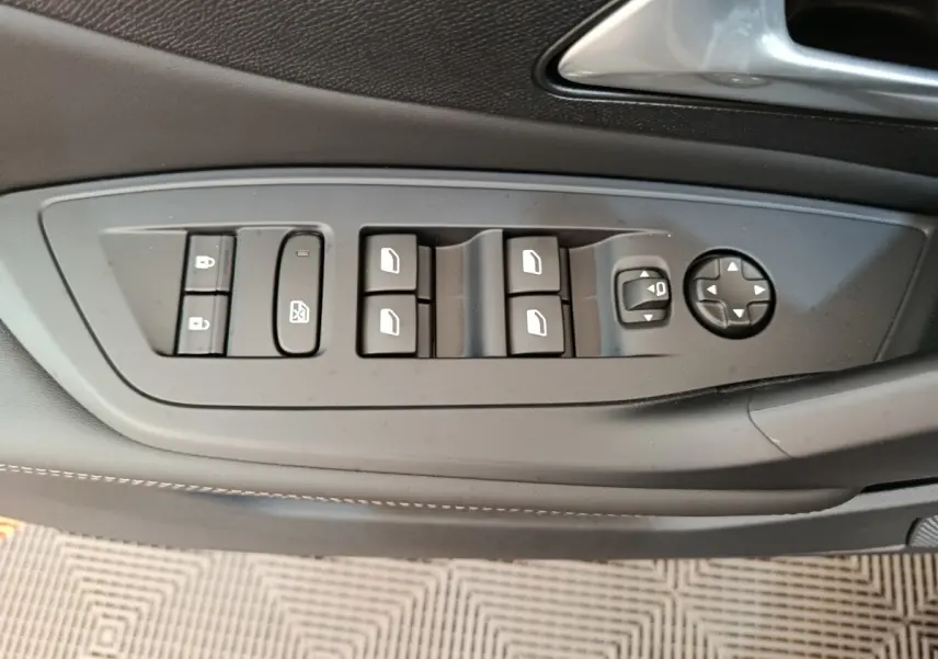 Gros plan sur les commandes de lève-vitres et rétroviseurs côté conducteur de la Peugeot 308 blanche 2026.