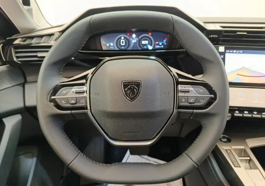 Vue rapprochée du volant cuir noir multifonctions de la Peugeot 308 2026 avec tableau de bord digital et écran tactile.