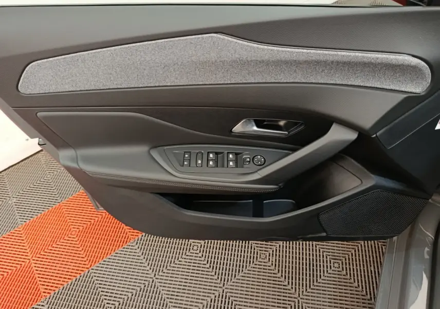 Vue intérieure côté gauche de la porte avant d'une Peugeot 308 blanche, avec commandes électriques et garniture grise.