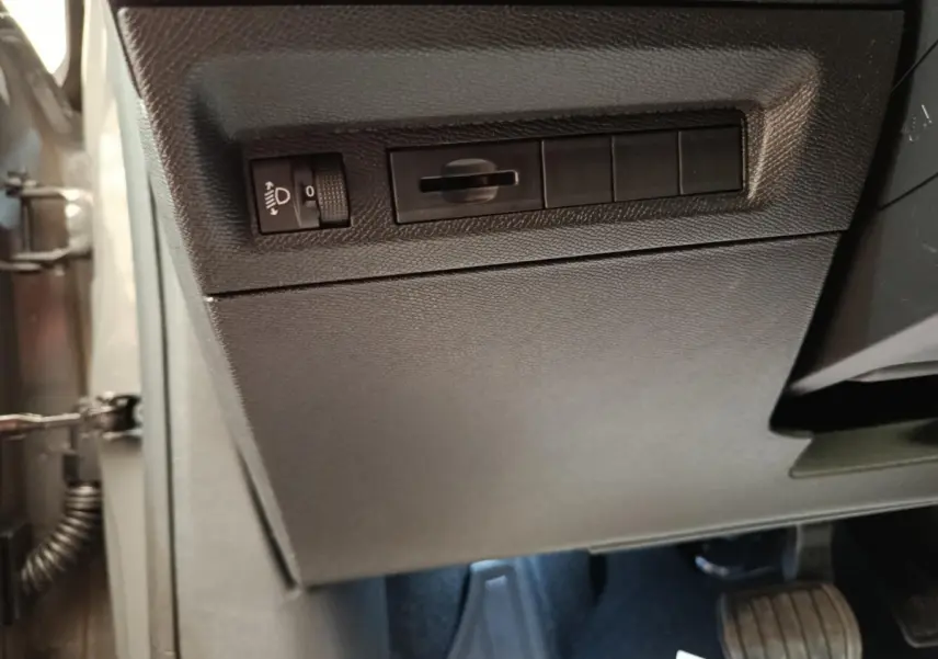 Vue intérieure côté conducteur de la Peugeot 308 blanche, montrant les commandes d'éclairage et les pédales.