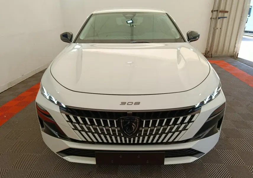 Vue avant d'une Peugeot 308 blanche 2026 avec calandre distinctive et phares LED fins allumés.