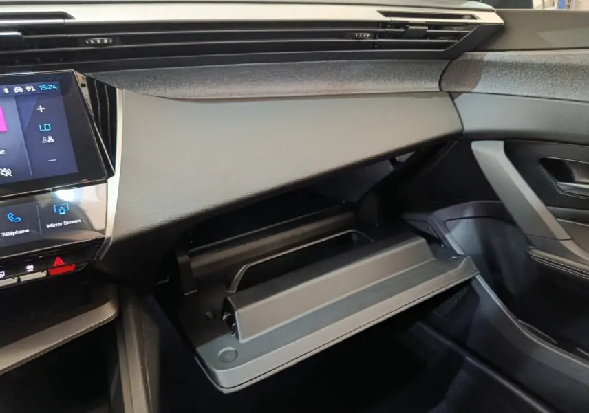 Vue intérieure côté passager de la Peugeot 308 2026 avec boîte à gants ouverte et tableau de bord noir.