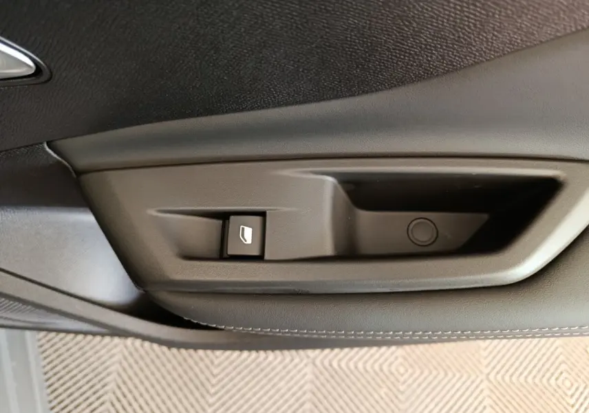 Gros plan sur la poignée intérieure noire de porte côté gauche de la Peugeot 308 blanche, avec bouton de commande de vitre.