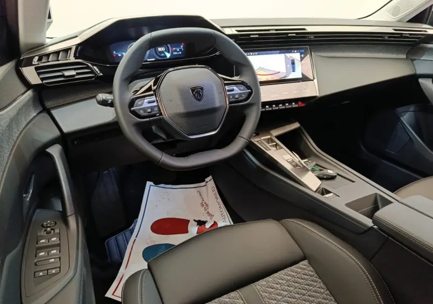 Vue intérieure côté conducteur du tableau de bord et volant cuir noir de la Peugeot 308 blanche 2026.