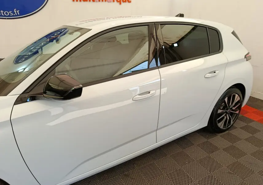 Vue latérale droite d'une Peugeot 308 blanche avec vitres teintées et jantes alliage noires et argentées.