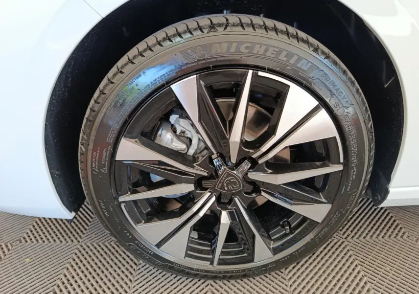 Gros plan sur la roue avant droite d'une Peugeot 308 blanche, jante alliage noire et argentée au design moderne.