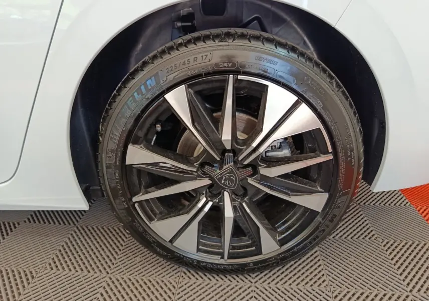 Gros plan sur la roue avant droite d’une Peugeot 308 blanche avec jante alliage noire et argentée au design moderne.