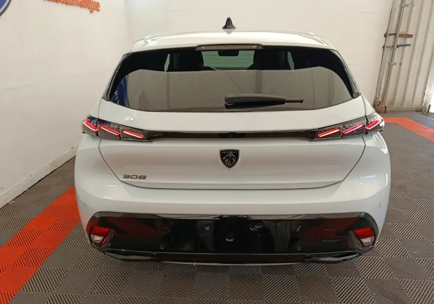 Vue arrière d'une Peugeot 308 blanche 2026 avec feux LED distinctifs et logo noir au centre du hayon.