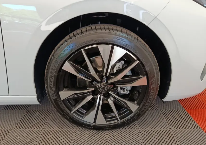 Gros plan sur la roue avant gauche de la Peugeot 308 blanche, avec jante alliage noire et argentée au design moderne.