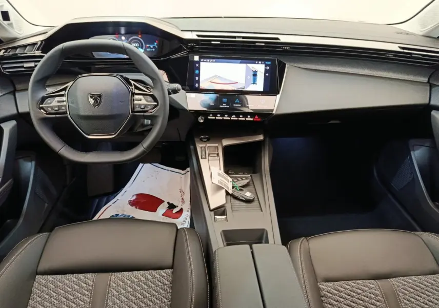 Intérieur de la Peugeot 308 2026 vue de face, volant cuir multifonctions et écran tactile central allumé.