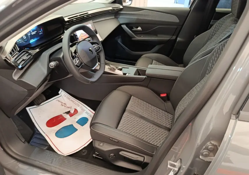 Vue intérieure côté conducteur de la Peugeot 308 blanche 2026, volant cuir multifonctions et sièges tissu-cuir gris.