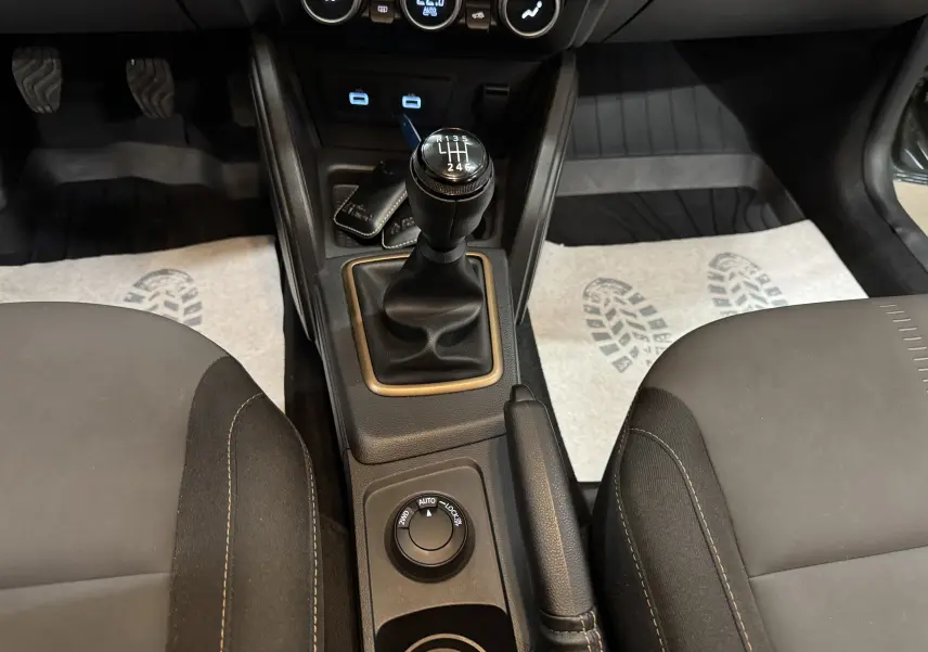 Vue intérieure centrée sur la console centrale du Dacia Duster 2024, montrant levier de vitesse manuel et commandes 4x4.