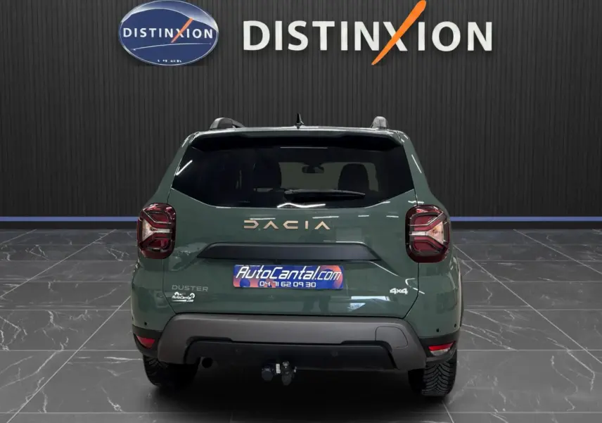 Vue arrière d'un Dacia Duster 2024 kaki lichen avec logo DACIA et attelage visible en intérieur showroom.