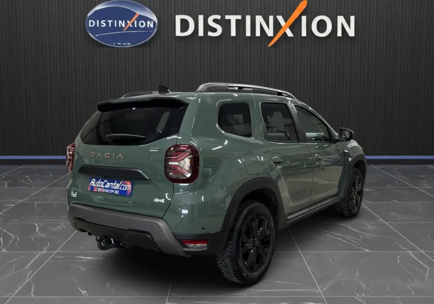 Vue 3/4 arrière droite du Dacia Duster 2024 kaki lichen avec jantes noires et attelage visible en intérieur showroom.