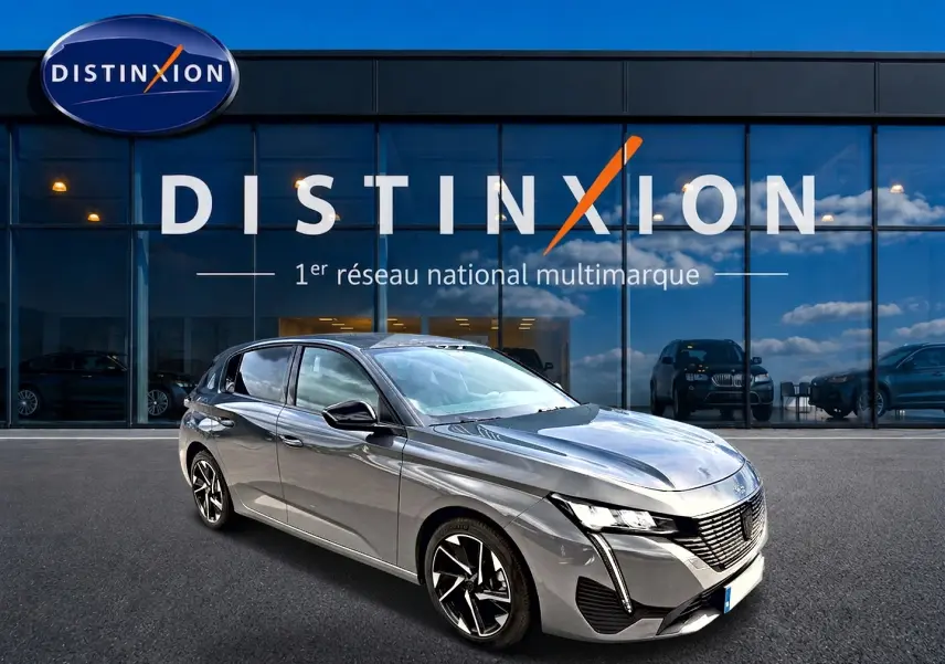 Peugeot 308 gris selenium en 3/4 avant droit, avec jantes alu et signature lumineuse LED distinctive.