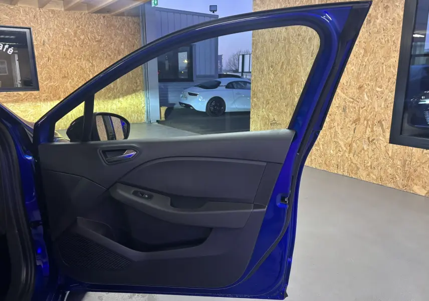 Porte avant gauche ouverte d’une Renault Clio bleu iron 2024, montrant l’intérieur gris noir et la poignée de porte.
