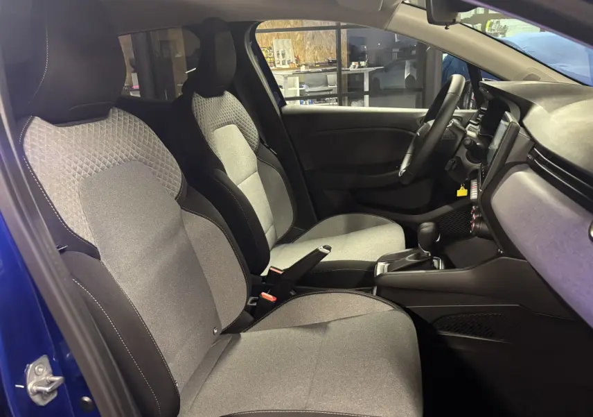 Intérieur de la Renault Clio 2024 bleu Iron, vue côté gauche, sièges tissu gris clair avec motifs géométriques et tableau de bord moderne.