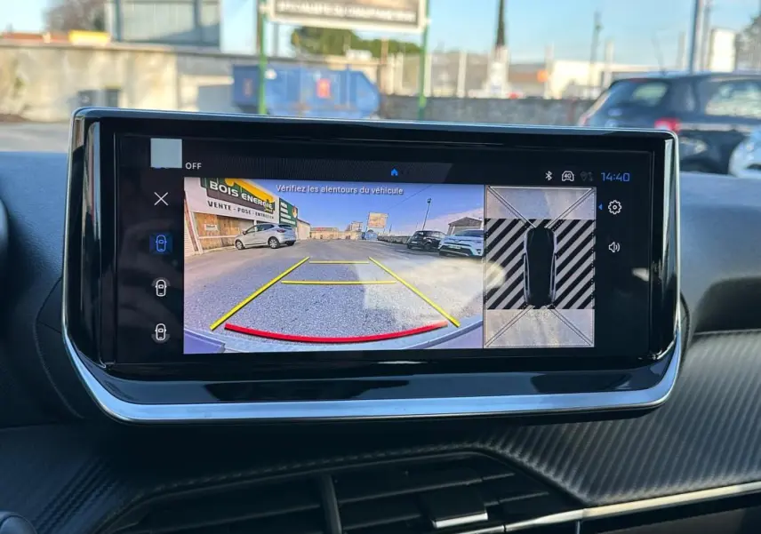 Écran tactile du cockpit numérique montrant la caméra de recul et vue 360° intérieure d'une Peugeot 208 blanche.