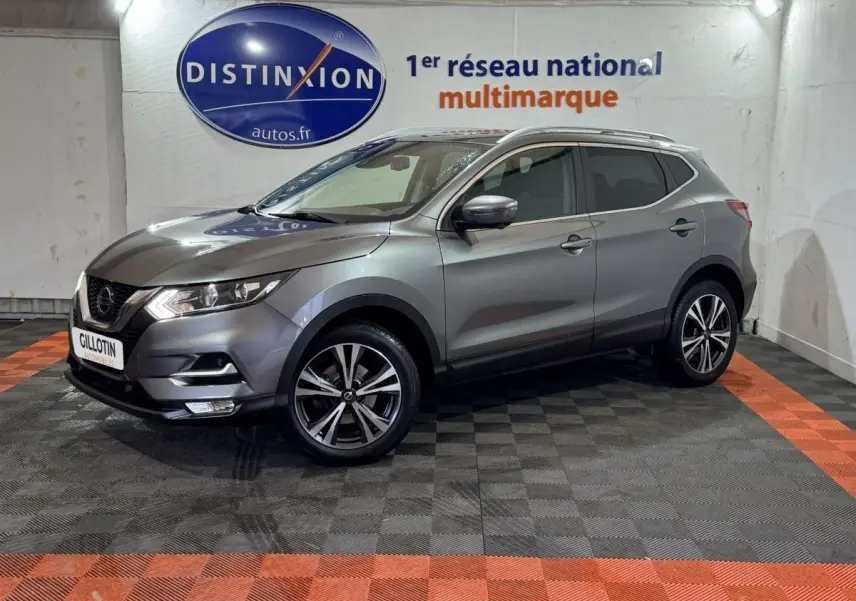 Nissan Qashqai gris foncé en 3/4 avant droit, avec jantes alliage et feux LED, dans un showroom intérieur.
