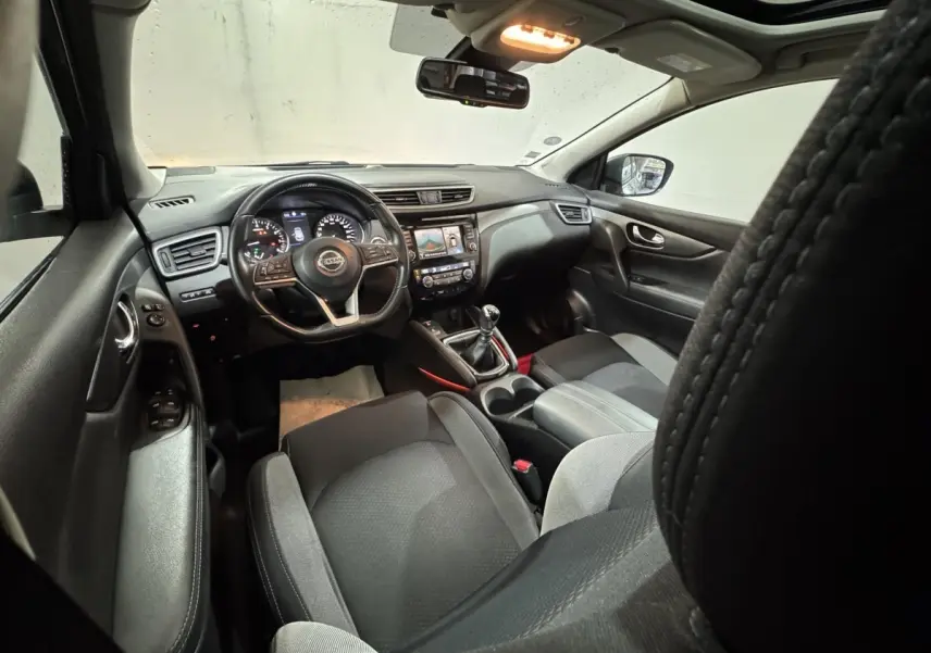 Vue intérieure avant du Nissan Qashqai 2019 gris foncé, volant cuir alu multifonctions et écran tactile central visible.