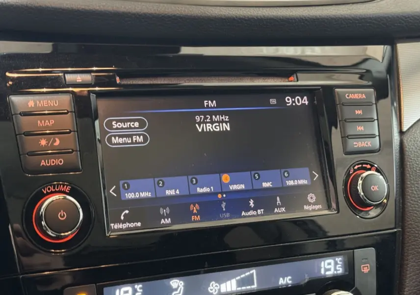 Gros plan sur l’écran tactile central noir du Nissan Qashqai gris foncé, affichant la radio FM et commandes audio.