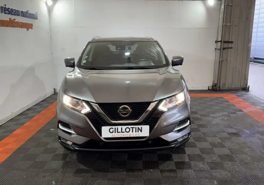 Vue frontale d'un Nissan Qashqai gris foncé avec phares allumés dans un garage éclairé.