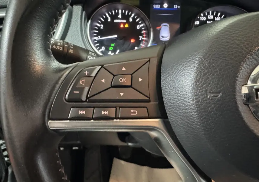 Gros plan sur le volant cuir et alu côté gauche du Nissan Qashqai gris foncé, avec commandes multifonctions et tableau de bord lumineux.