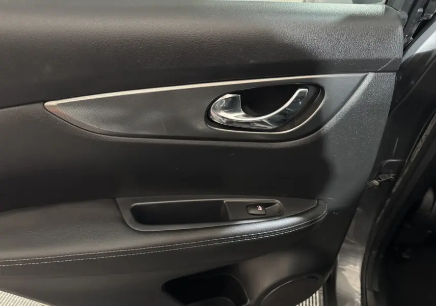 Gros plan sur la porte intérieure côté gauche du Nissan Qashqai gris foncé, avec poignée chrome et bouton de verrouillage.