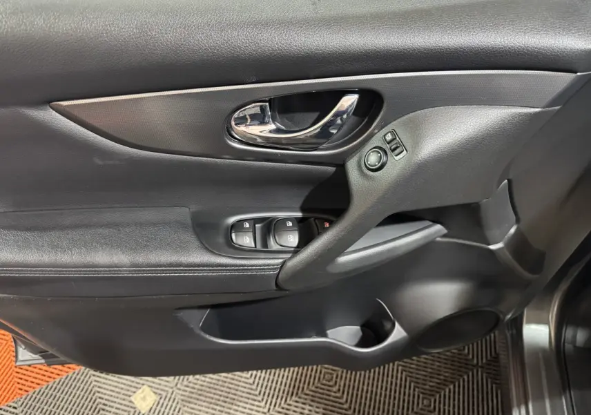 Gros plan sur la porte intérieure côté conducteur du Nissan Qashqai gris foncé, avec commandes de vitres et poignée chromée.