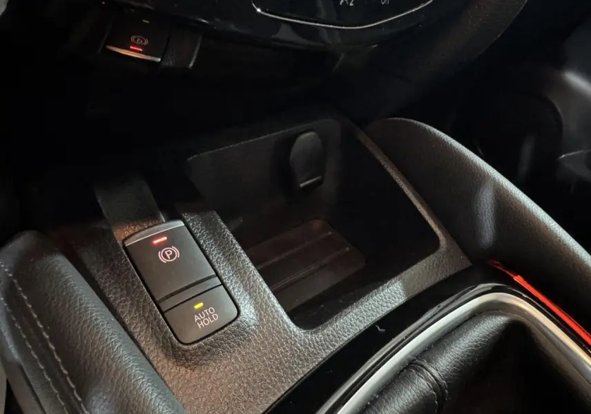 Gros plan sur la console centrale du Nissan Qashqai gris foncé, montrant le frein à main électrique et le bouton Auto Hold.