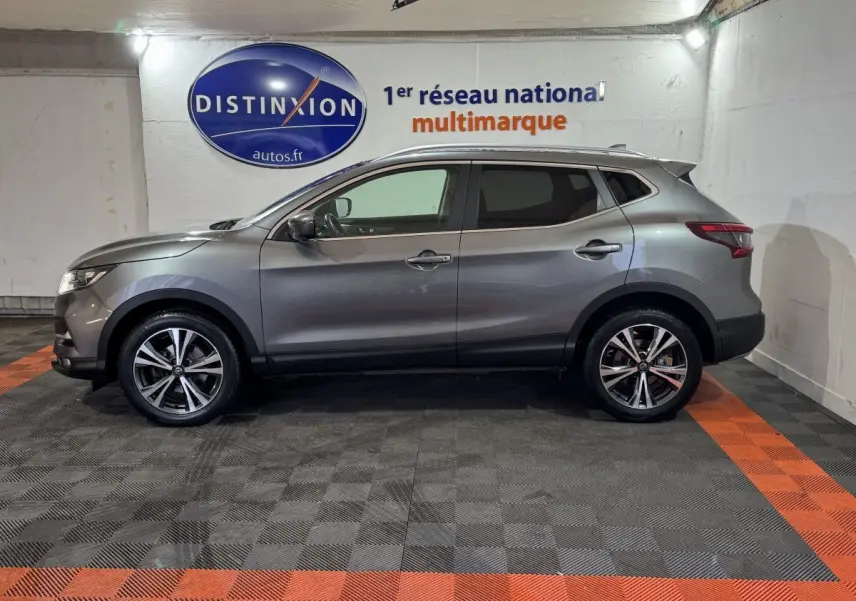 Profil droit d'un Nissan Qashqai gris foncé 2019, avec jantes alliage et vitres teintées, en intérieur showroom.