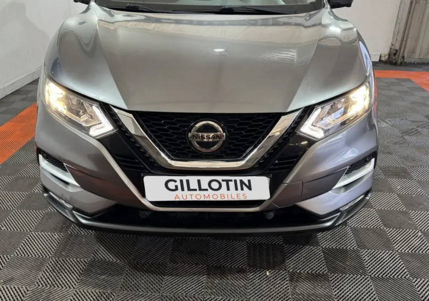 Vue avant du Nissan Qashqai gris foncé 2019 avec phares allumés et calandre chromée distinctive.