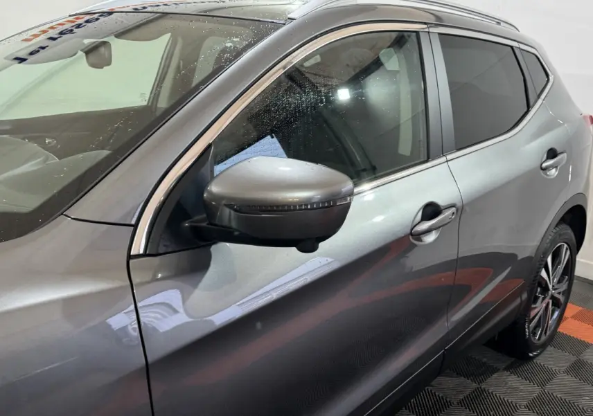 Vue côté gauche avant d'un Nissan Qashqai gris foncé 2019 avec rétroviseur et jante alliage visibles.