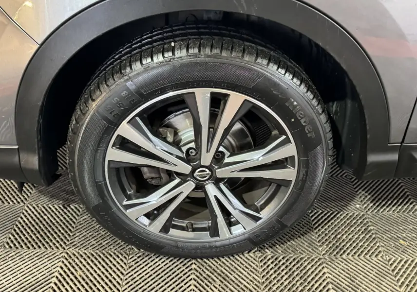 Gros plan sur la roue avant droite du Nissan Qashqai gris foncé, mettant en valeur la jante alu à design moderne.