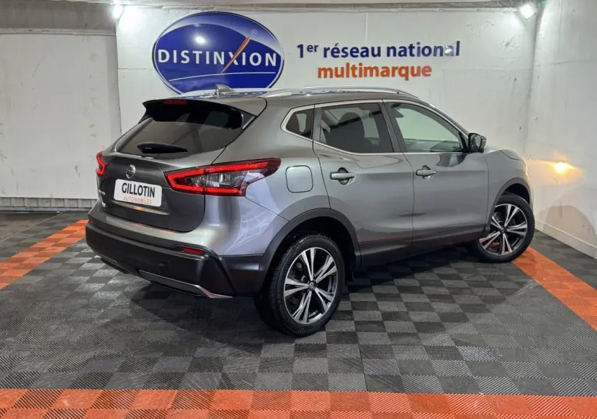 Vue 3/4 arrière droite d'un Nissan Qashqai gris foncé avec jantes alliage et feux arrière LED, en intérieur showroom.