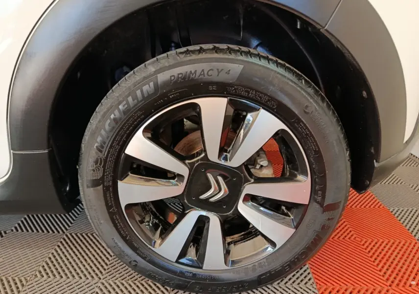 Gros plan sur la roue avant droite d'une Citroën C3 blanche, jante alliage bicolore avec logo Citroën au centre.