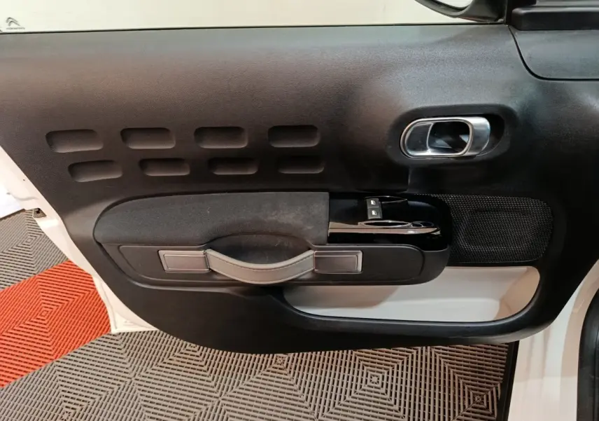 Vue rapprochée de la porte avant gauche blanche d'une Citroën C3 2021 avec poignée noire et commandes de vitres.