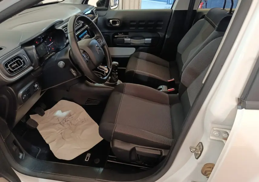 Vue intérieure côté conducteur d'une Citroën C3 blanche 2021 avec sièges tissu noirs et volant cuir multifonctions.