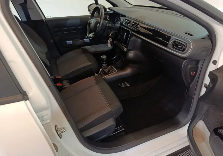 Intérieur avant droit d'une Citroën C3 blanche 2021, montrant sièges tissu, volant cuir et tableau de bord noir brillant.